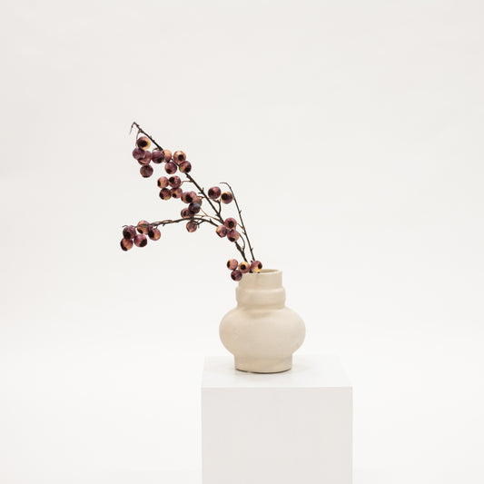 White vase with dried branches on a white pedestal against a white background