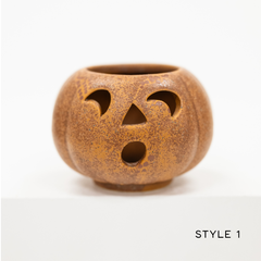 A small pumpkin-shaped ceramic candle holder with carved jack-o'-lantern facial cutouts, shown on a clean white background with the text 'STYLE 1' in the bottom right corner.
