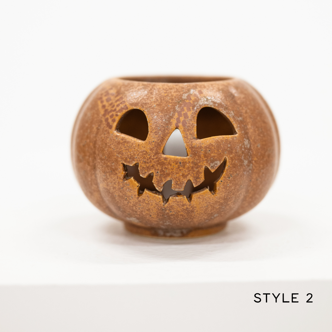 A small pumpkin-shaped ceramic candle holder with a carved jack-o'-lantern face, shown on a white background with the text 'STYLE 2' in the bottom right corner.