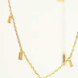 Gold necklace with small cylindrical pendants on a light background