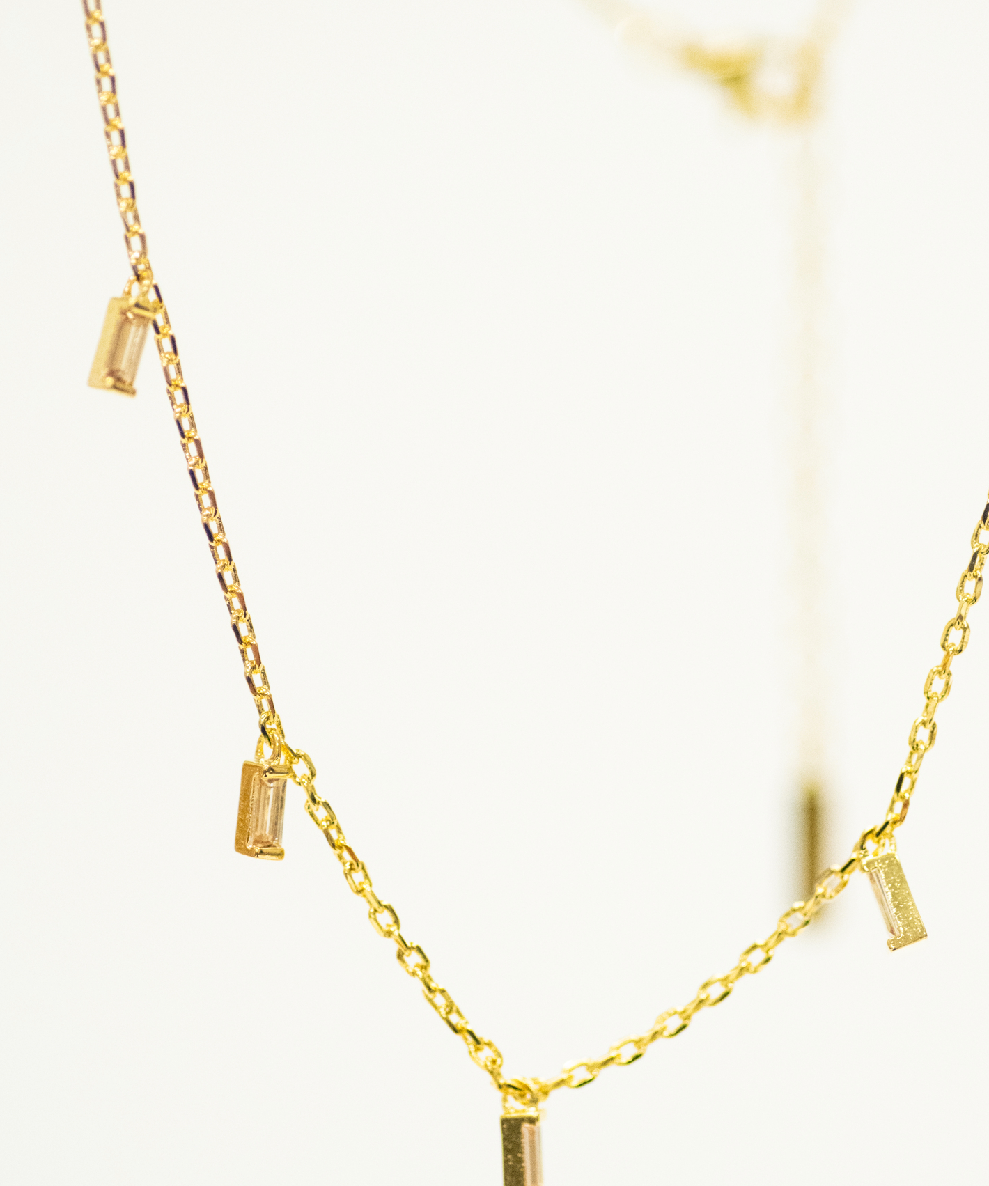 Gold necklace with small cylindrical pendants on a light background