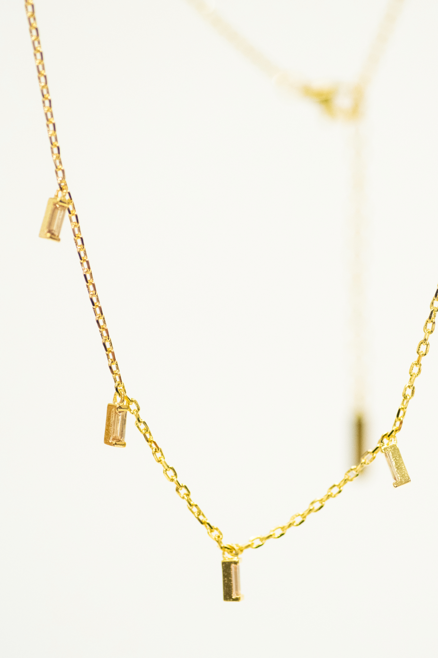 Gold necklace with small cylindrical pendants on a light background