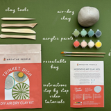 Meditative art clay kit with tools, air-dry clay, acrylic paints, and a resealable bag on a green background.