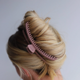Pink hair clip in a person's blonde hair against a white background