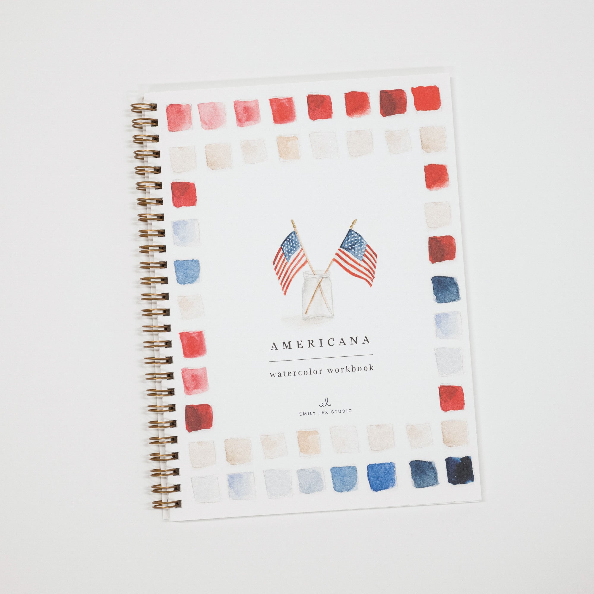 A spiral-bound watercolor workbook titled 'AMERICANA' with a white cover, decorated with a border of red, white, and blue watercolor paint swatches and two small American flags near the center. The brand 'Emily Lee Studio' is printed at the bottom.