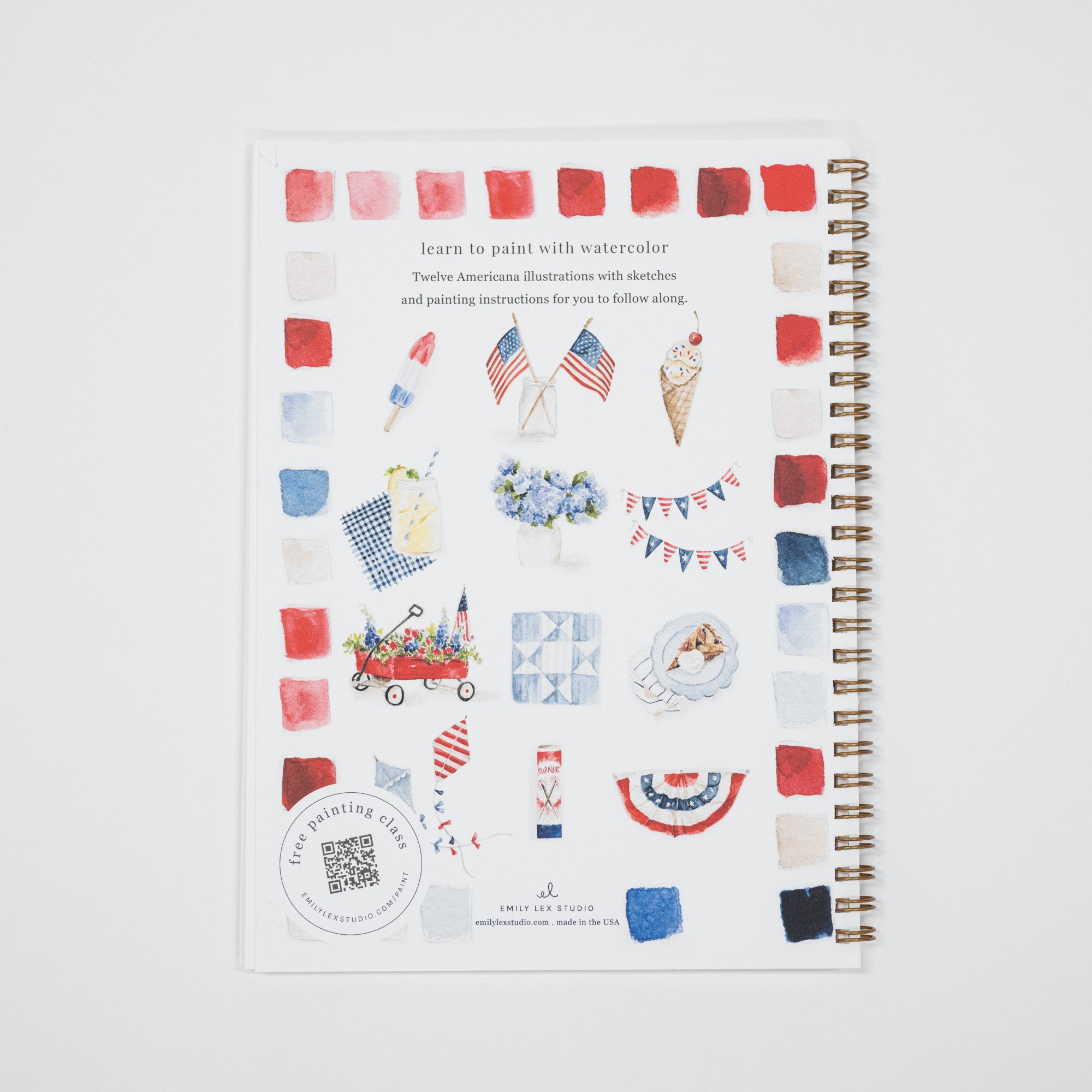 A spiral-bound watercolor painting guide book with a patriotic red, white, and blue theme, featuring illustrations of American flags, an ice cream cone, a wagon, and bunting on a white cover.