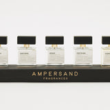 Five Ampersand Fragrances bottles on a black stand with a white background