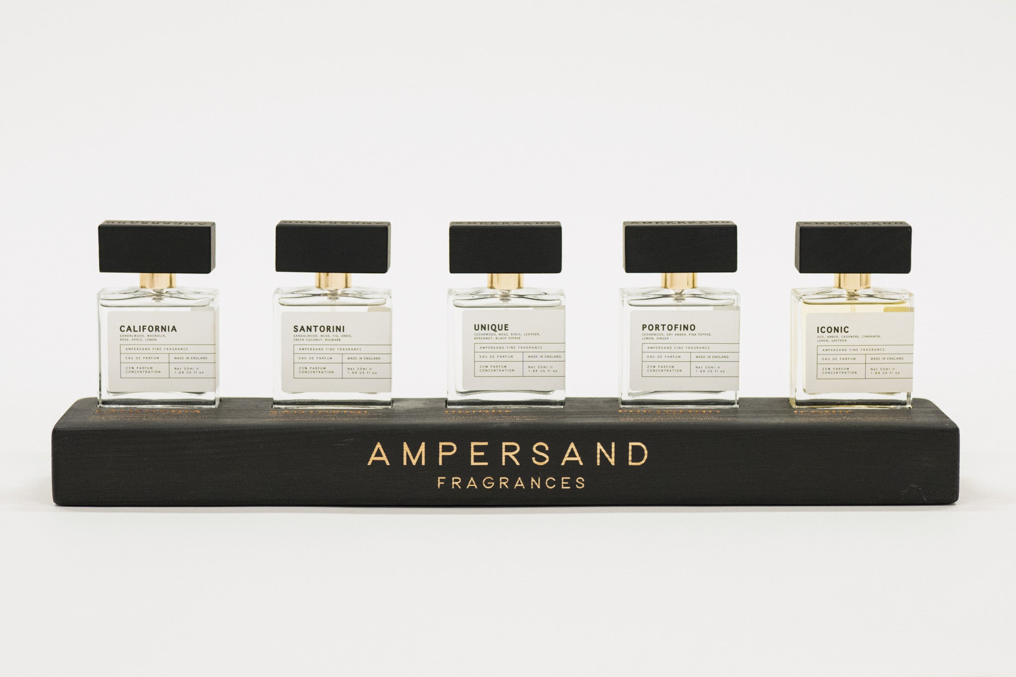 Five Ampersand Fragrances bottles on a black stand with a white background