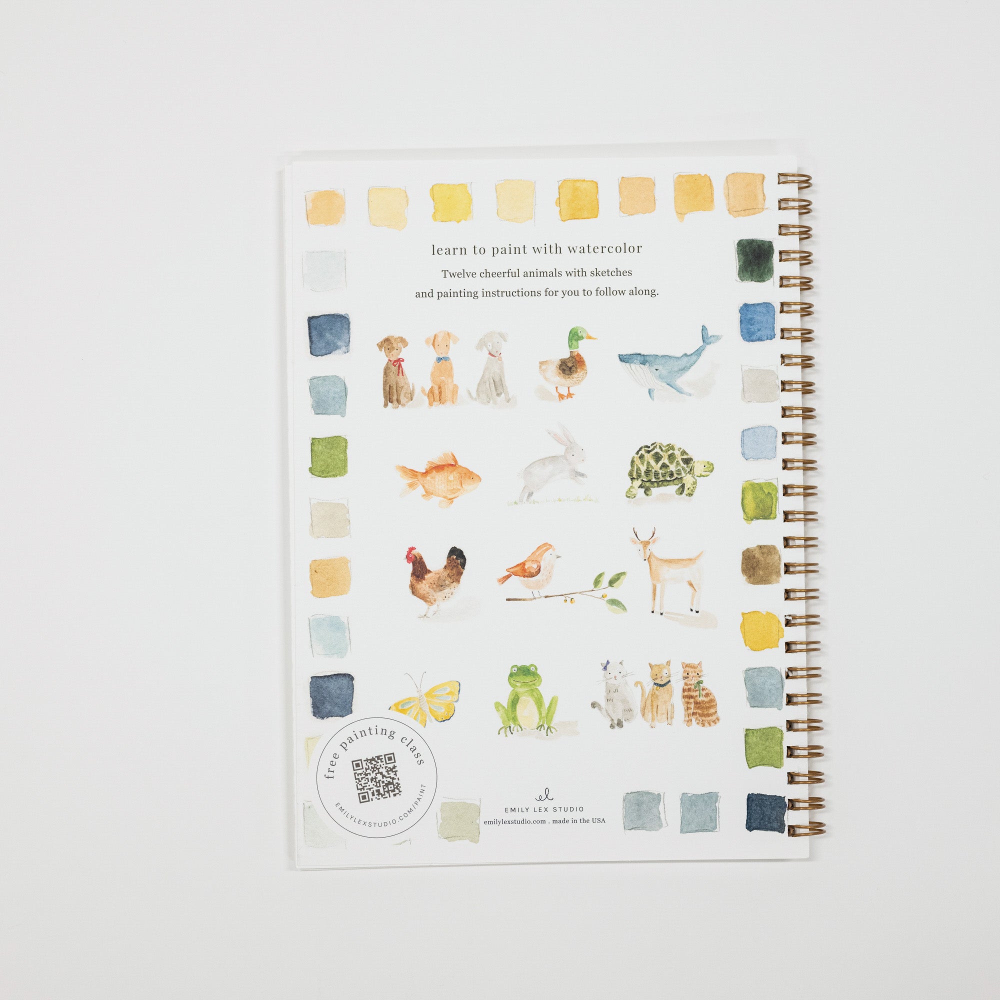 A spiral-bound watercolor painting guide book with animal illustrations and color swatches, photographed flat against a light gray background.