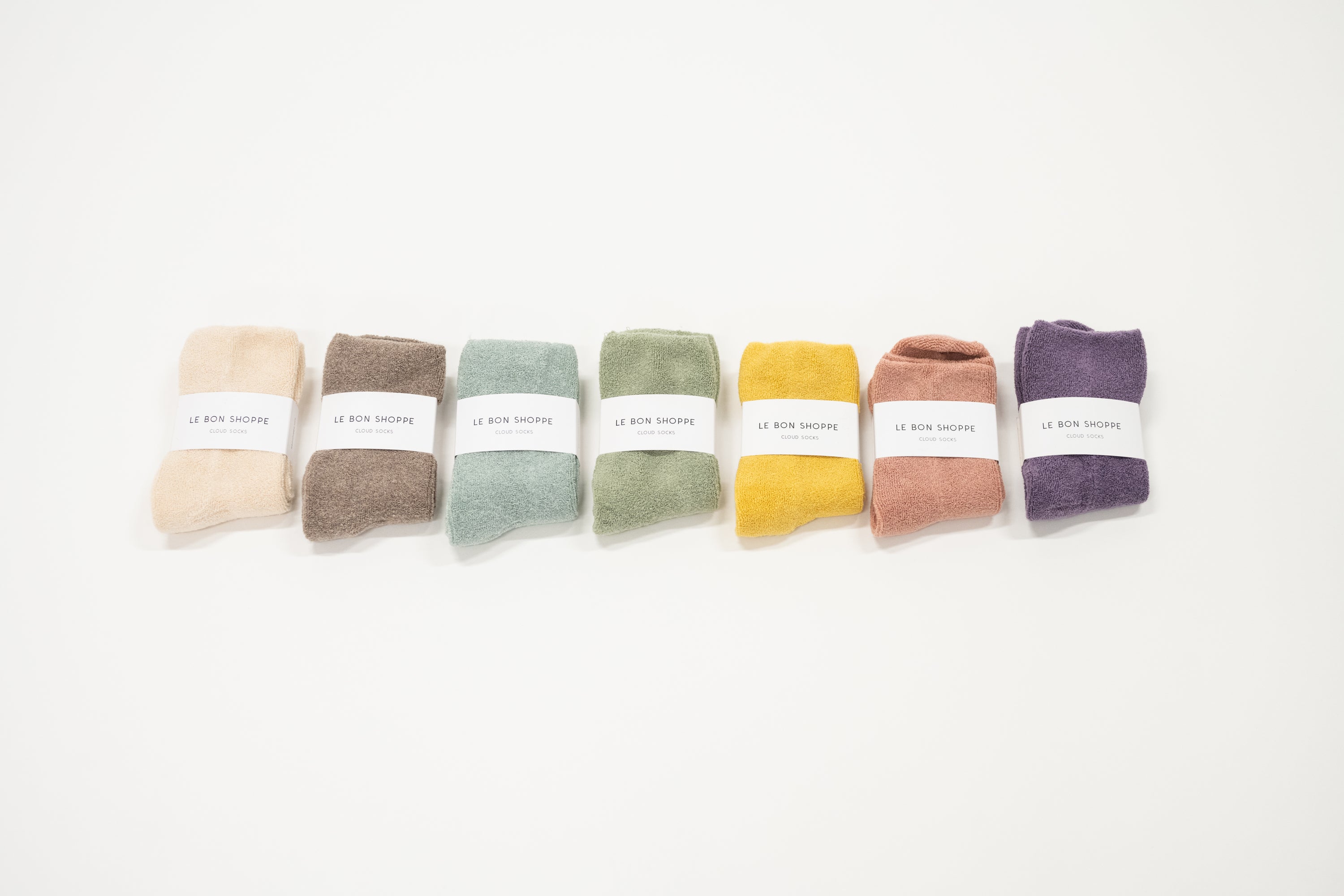 7 different colored cloud socks on a white surface, each with a label indicating the brand le bon shoppe