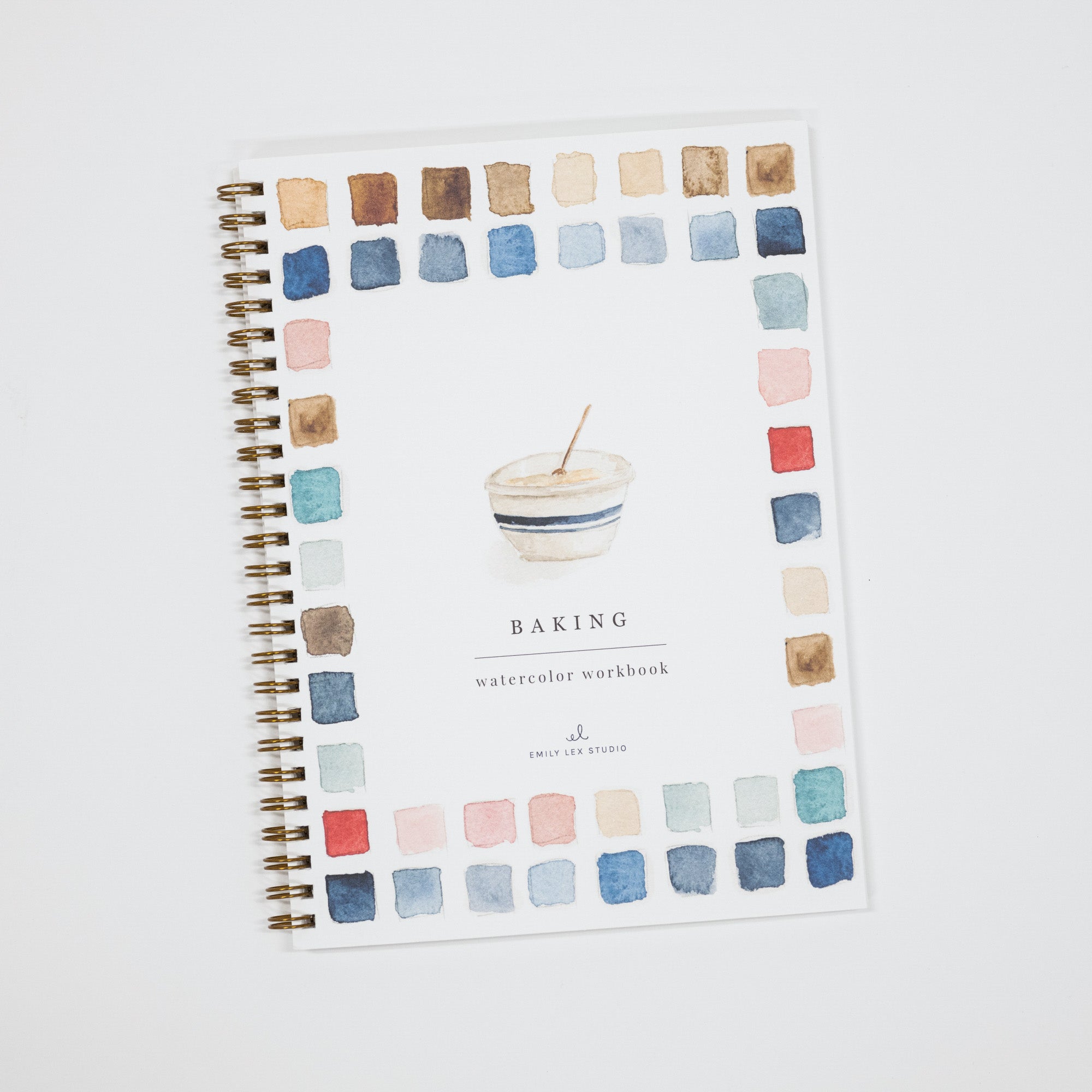 A spiral-bound watercolor workbook titled 'BAKING' with a watercolor bowl illustration in the center and a border of multicolored paint swatches around the edges, photographed on a light gray background.