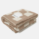 A folded fleece throw blanket with a beige and cream checkerboard pattern, featuring a white paper label that reads 'ARCTIC FOX'.