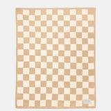 A square knit blanket featuring a beige and cream checkerboard pattern, displayed flat against a light gray background with a small brand label in the bottom right corner.
