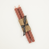 pink braided candles tied with a paper wrap on a white background
