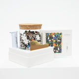Jigsaw puzzle pieces in a container with a wooden lid on a white surface