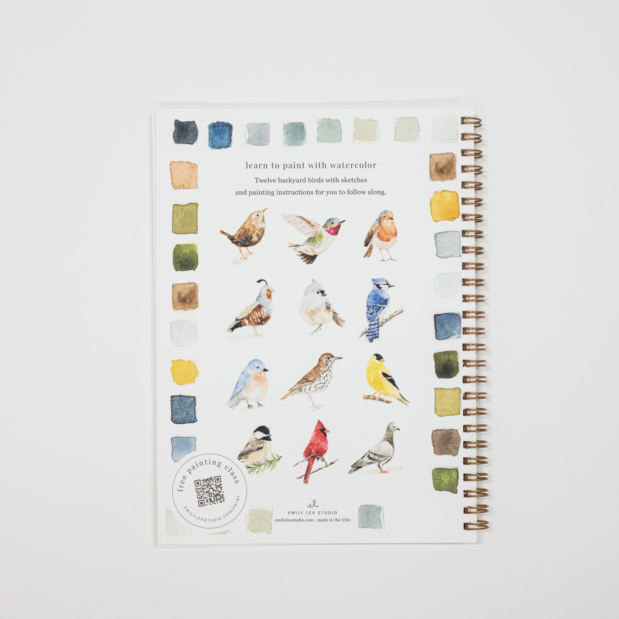 A spiral-bound notebook featuring watercolor bird illustrations and small paint swatches on the cover, photographed against a clean white background.