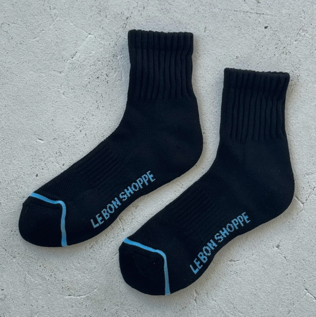 Pair of black socks with 'Le Bon Shoppe' branding on a gray surface