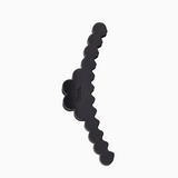 A single black hair accessory with a wavy, scalloped edge and a small embossed logo, shown on a plain light gray background.