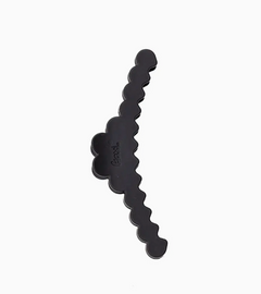 A single black hair accessory with a wavy, scalloped edge and a small embossed logo, shown on a plain light gray background.