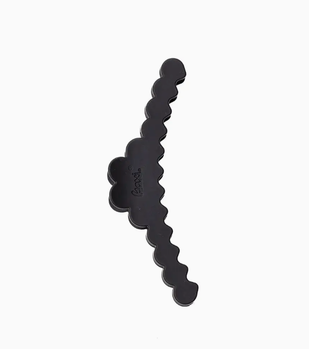 A single black hair accessory with a wavy, scalloped edge and a small embossed logo, shown on a plain light gray background.
