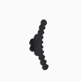 A black hair clip with a wavy, scalloped edge and a small embossed brand name, shown on a plain white background.