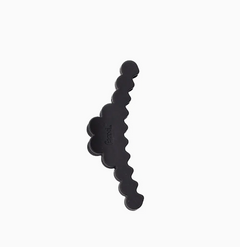 A black hair clip with a wavy, scalloped edge and a small embossed brand name, shown on a plain white background.