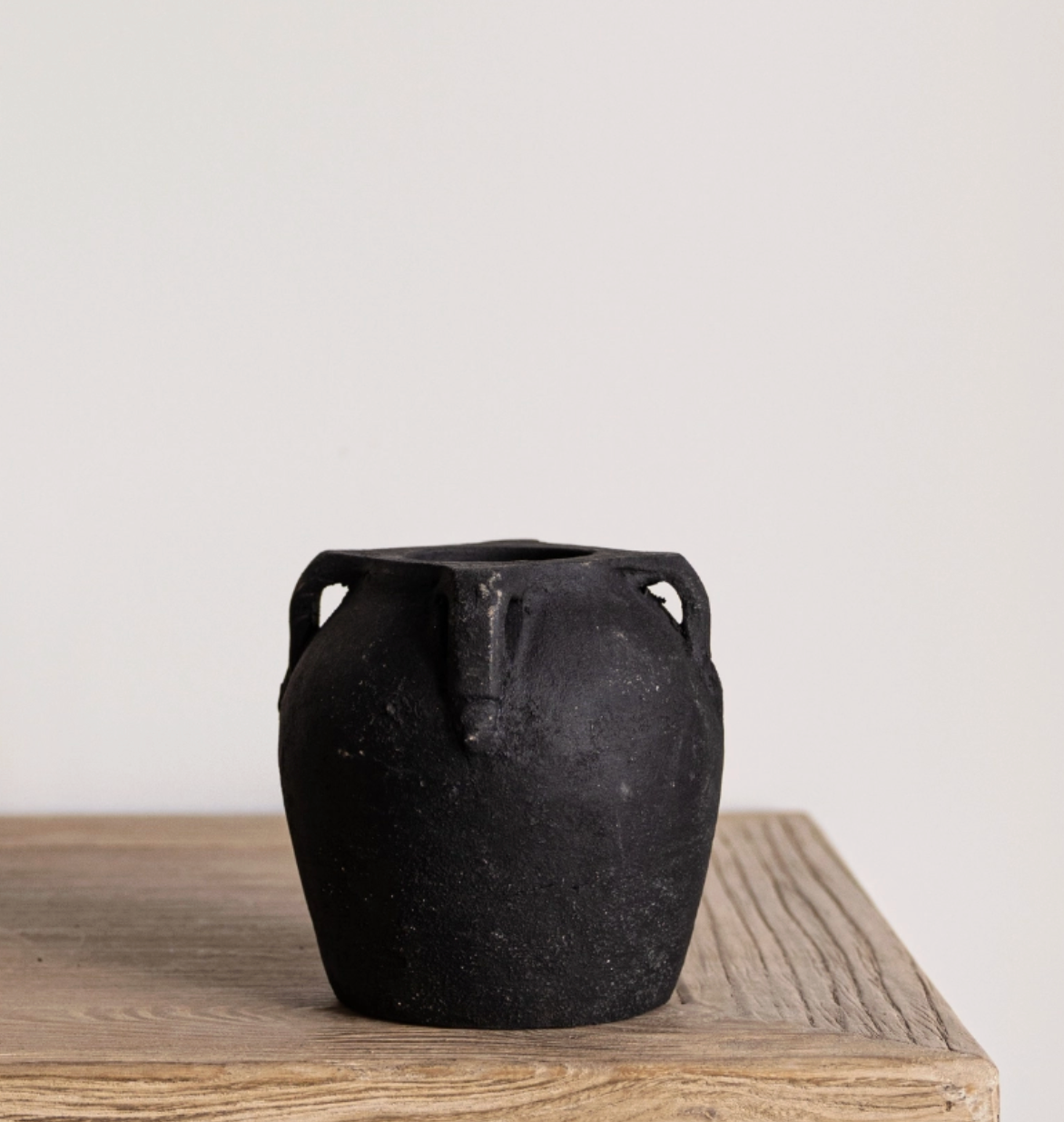 a small black vase with four handles and a chalky finish