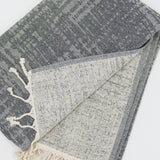 Gray black beach towel with white tassels on a light gray background