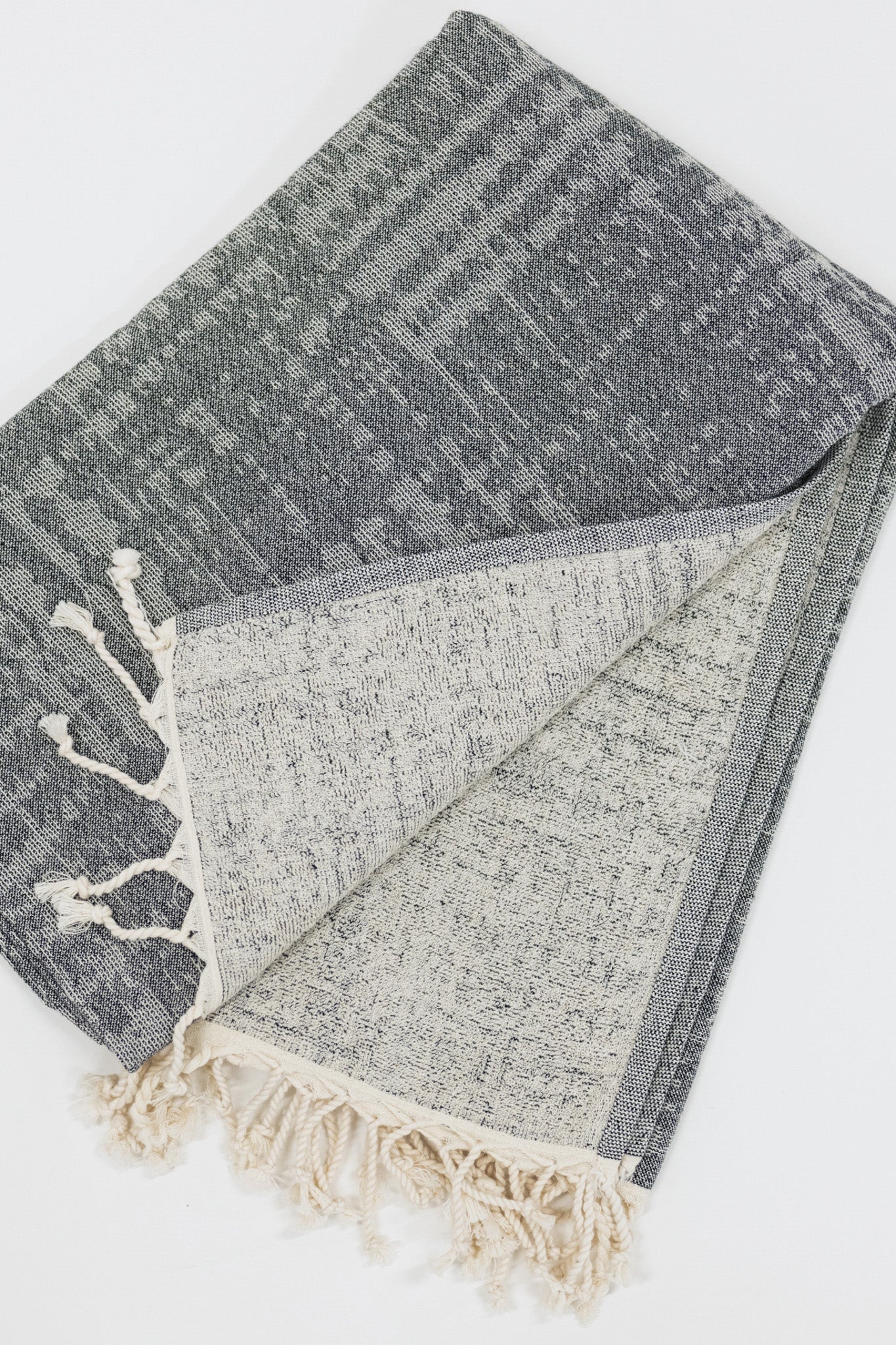 Gray black beach towel with white tassels on a light gray background