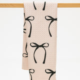 Beige towel with black bow pattern hanging on a wooden rack.