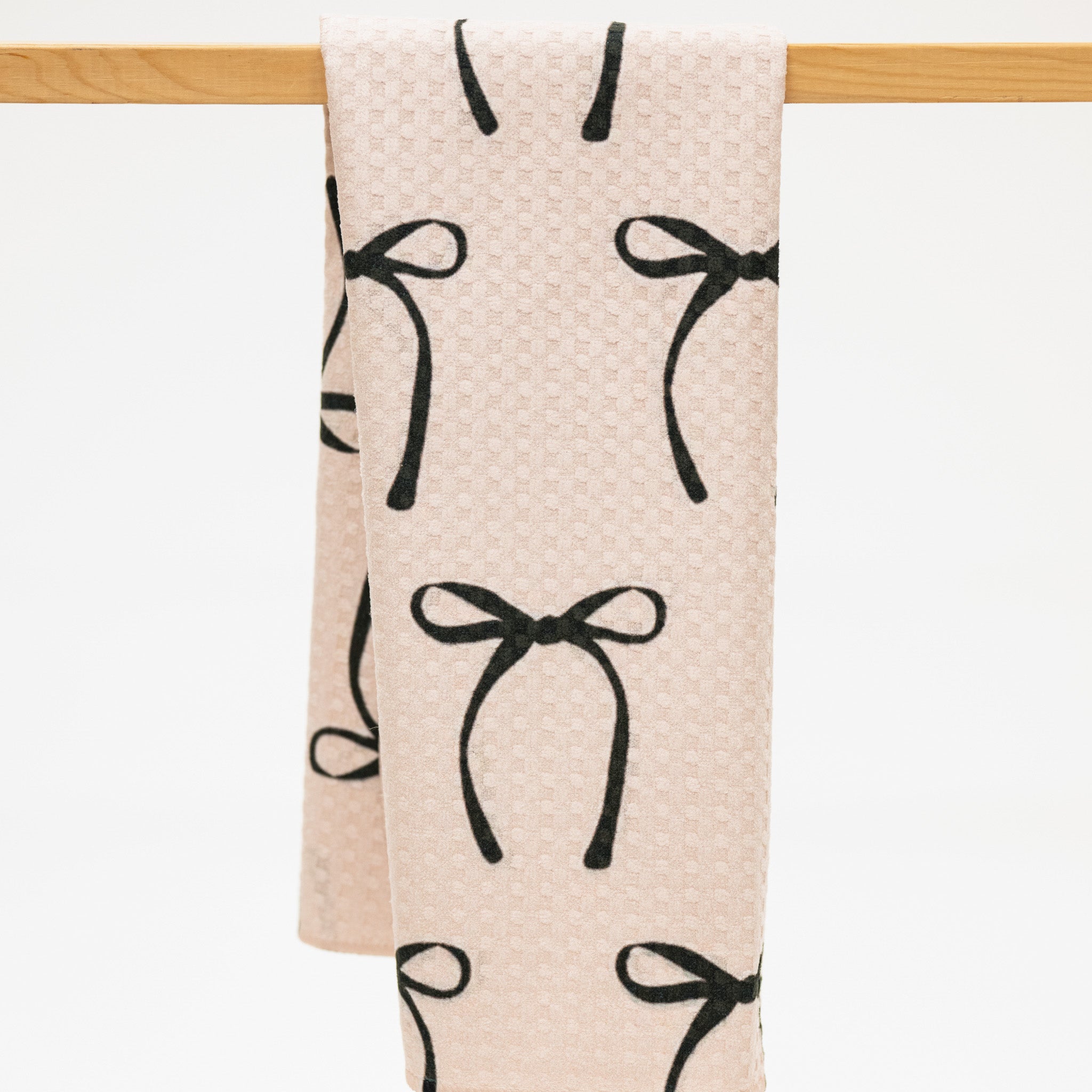 Beige towel with black bow pattern hanging on a wooden rack.