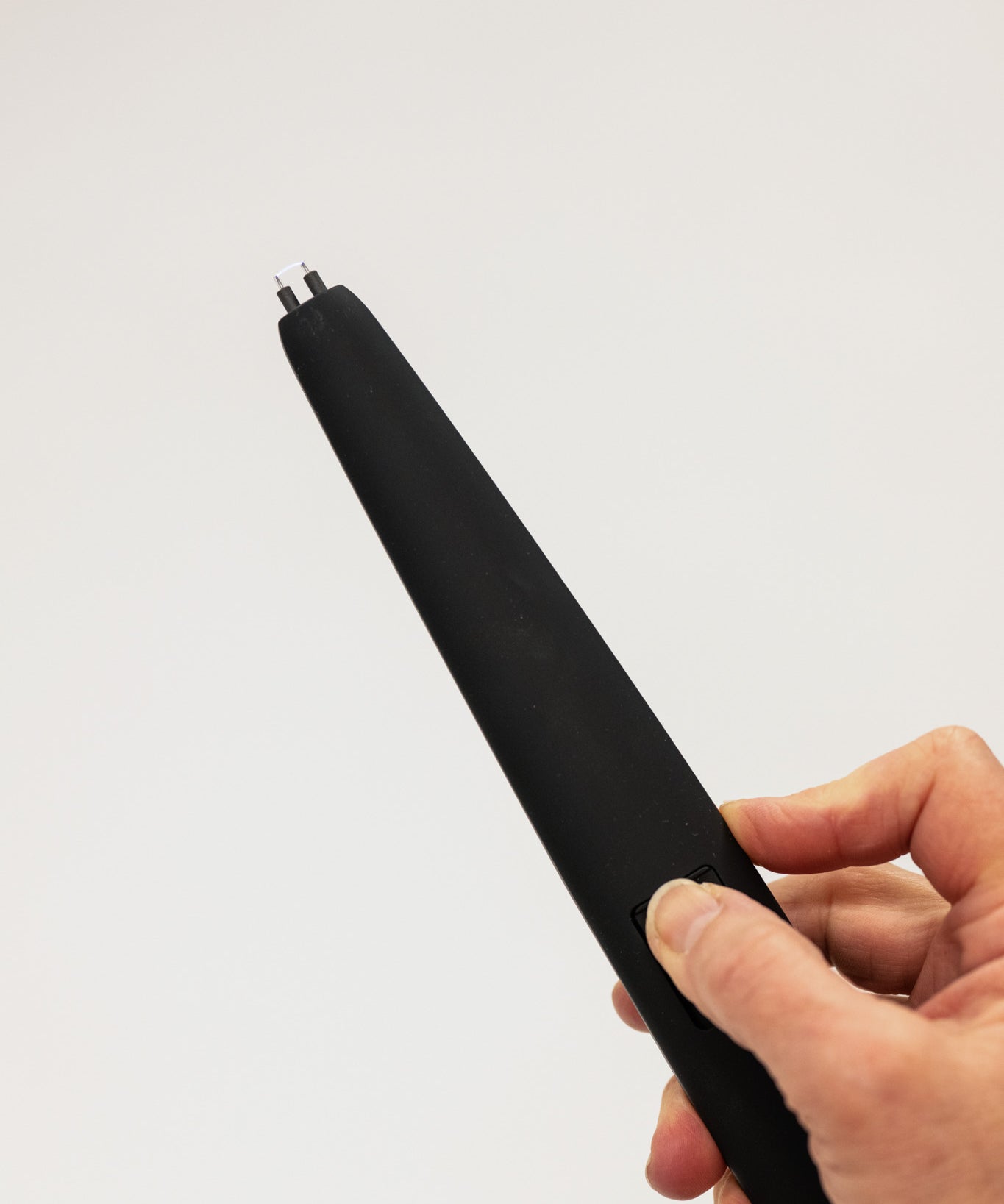 Black electronic device held in a hand against a light gray background