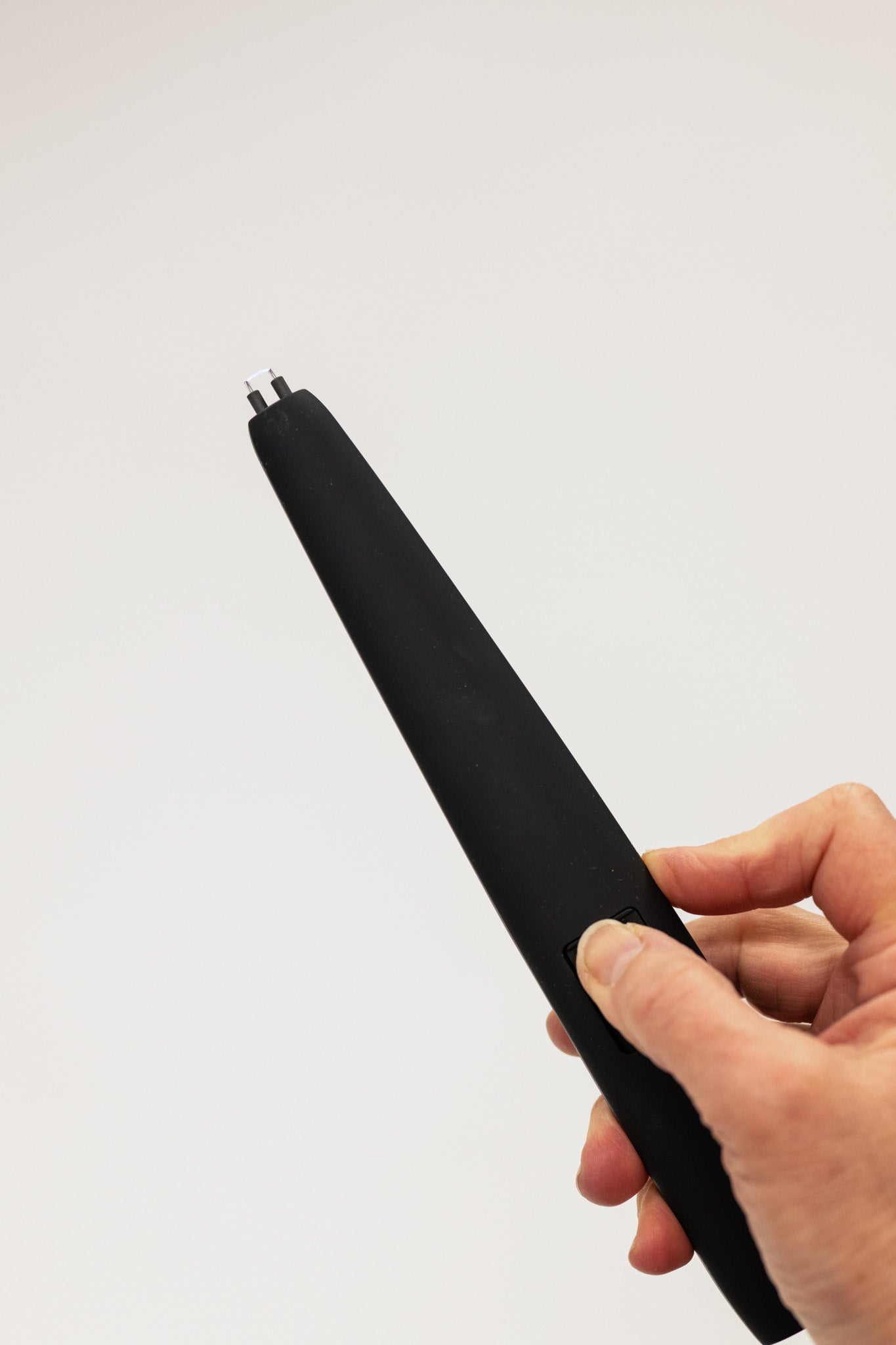 Black electronic device held in a hand against a light gray background