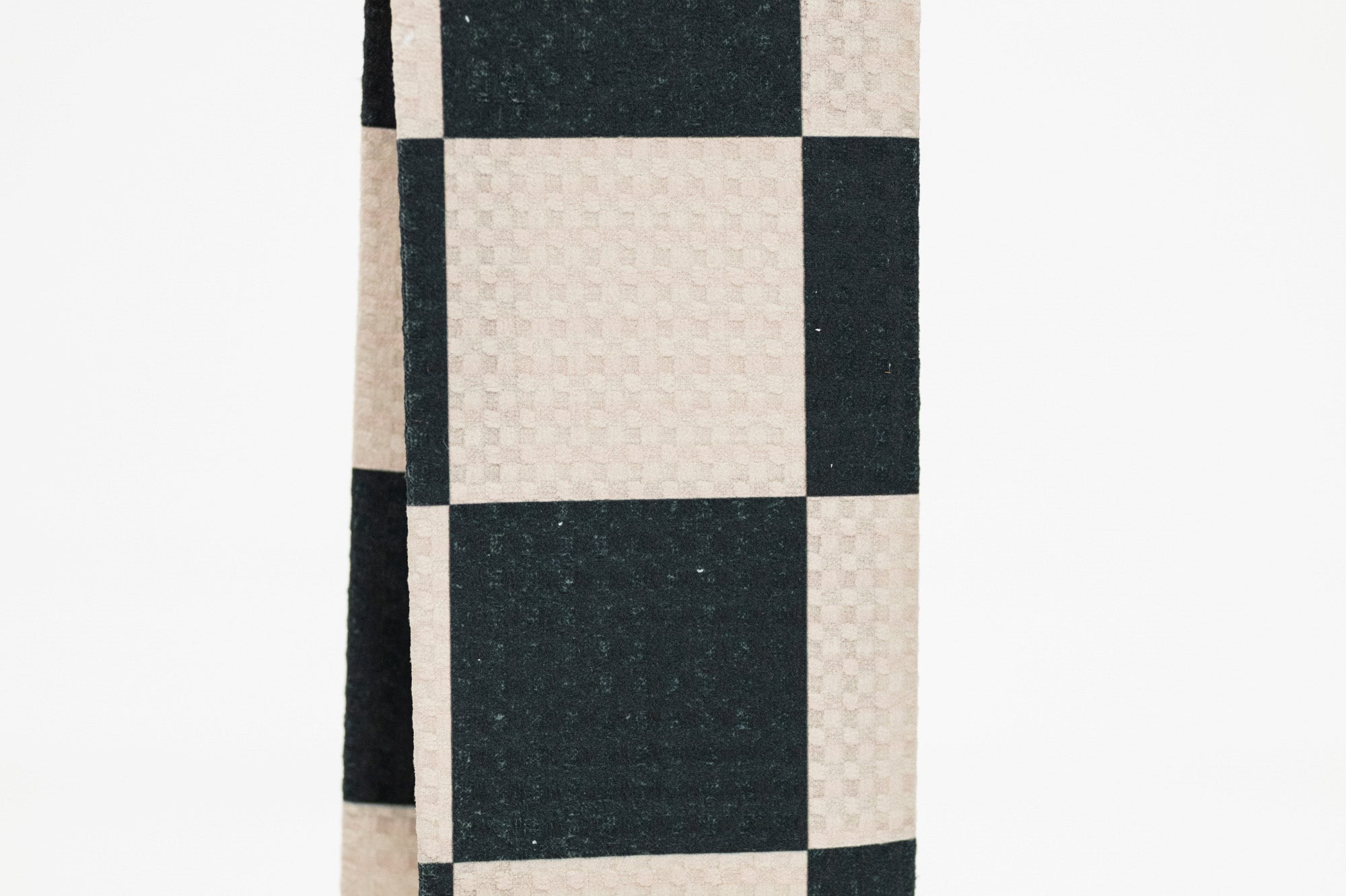 A close-up of a checkered fabric pattern with alternating black and warm off-white squares, showing a subtle woven texture.