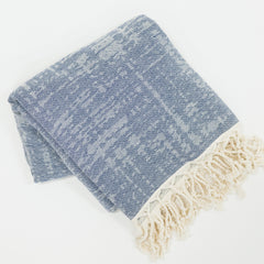 Folded blue and white beach towel with tassels on a light gray background