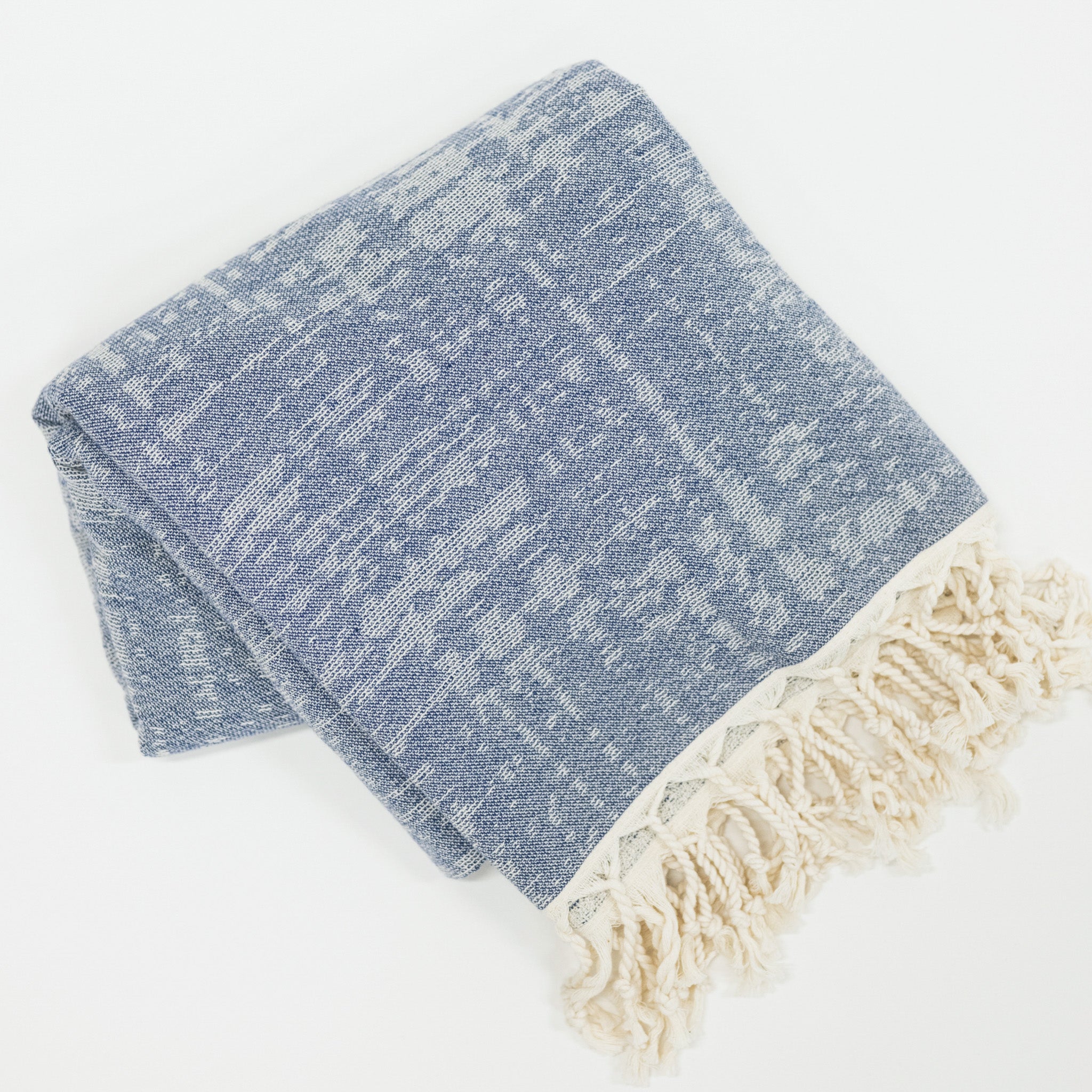 Folded blue and white beach towel with tassels on a light gray background