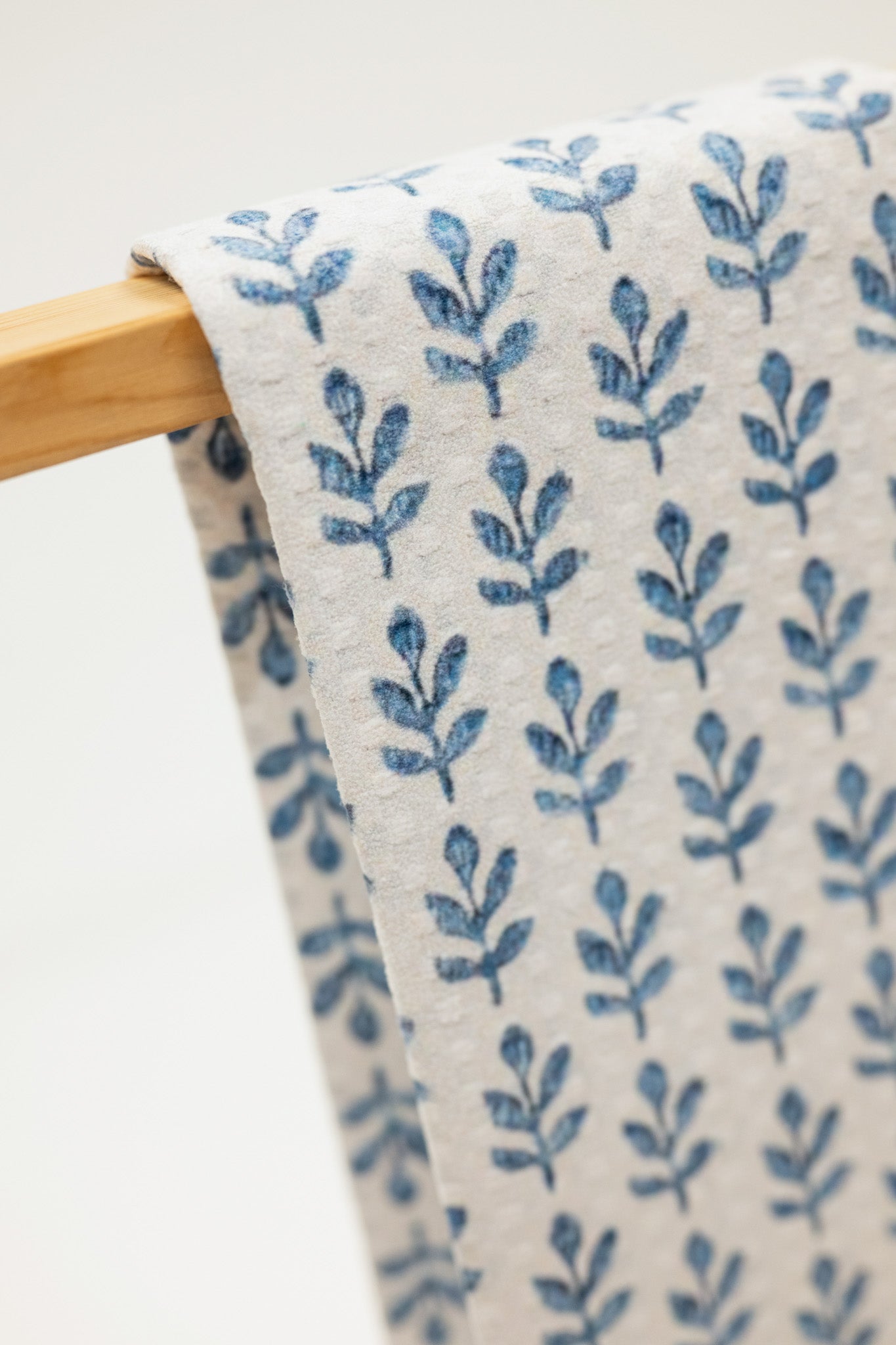 Fabric with blue leaf pattern on a wooden hanger against a white background