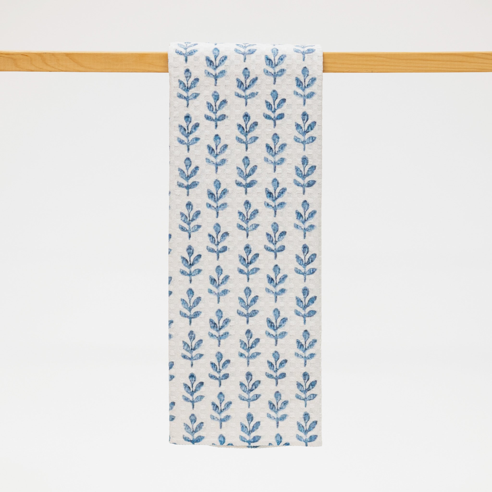 Blue floral patterned towel hanging on a wooden rod against a white background