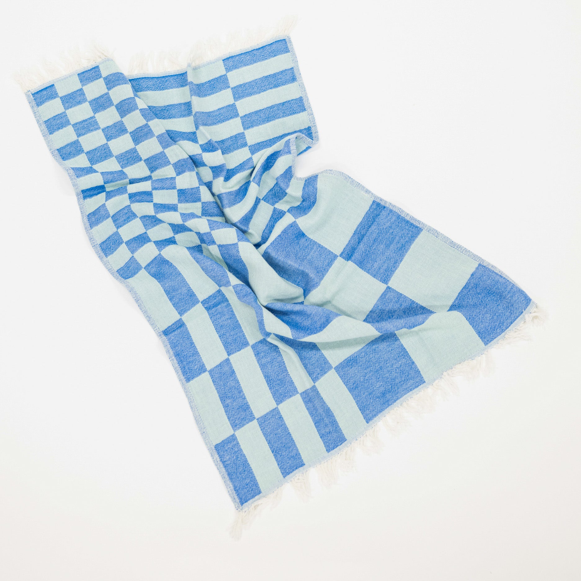 A woven kitchen towel with a blue and light blue checkerboard pattern and fringed edges, laid out on a clean white background.