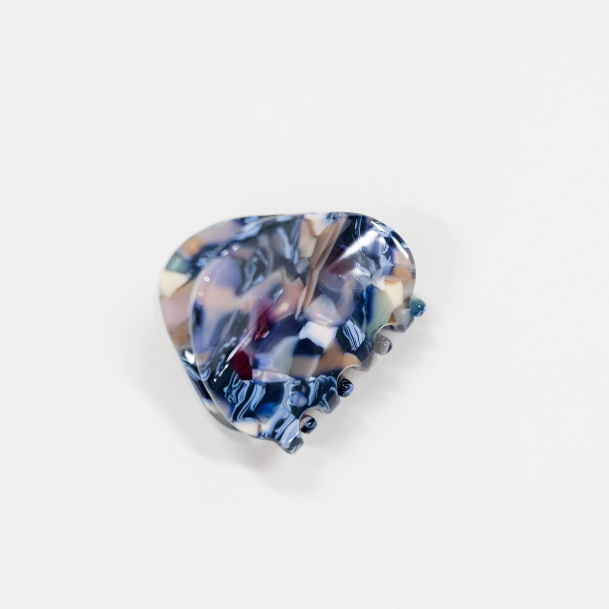 A single glossy hair claw clip with a marbled shell-like pattern in navy blue, beige, white, and hints of purple, shown on a plain light gray background.