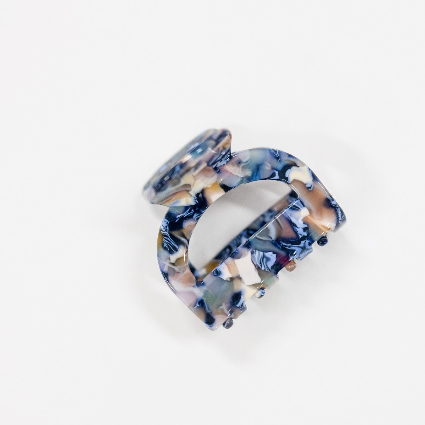 A single hair claw clip made of glossy marbled resin, featuring a swirl pattern of navy blue, beige, white, and light purple, photographed on a seamless white background.