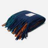 A folded woolen scarf with a gradient color transition from deep navy blue to teal and rust orange, featuring a white woven label that reads 'arctic fox'.