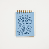 A small spiral-bound notebook with a light blue cover featuring dark blue dog illustrations, photographed against a plain white background.