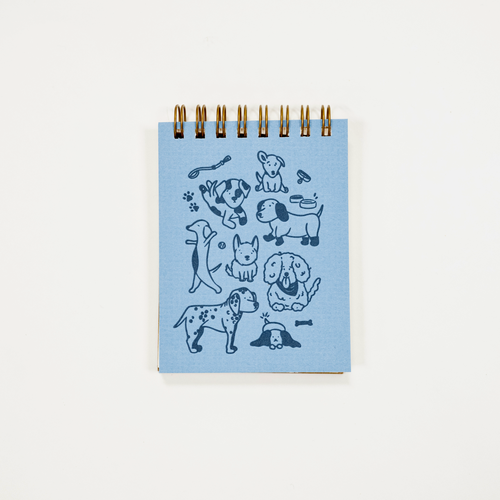 A small spiral-bound notebook with a light blue cover featuring dark blue dog illustrations, photographed against a plain white background.