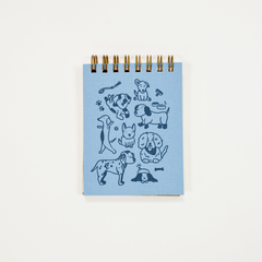 A small spiral-bound notebook with a light blue cover featuring dark blue dog illustrations, photographed against a plain white background.