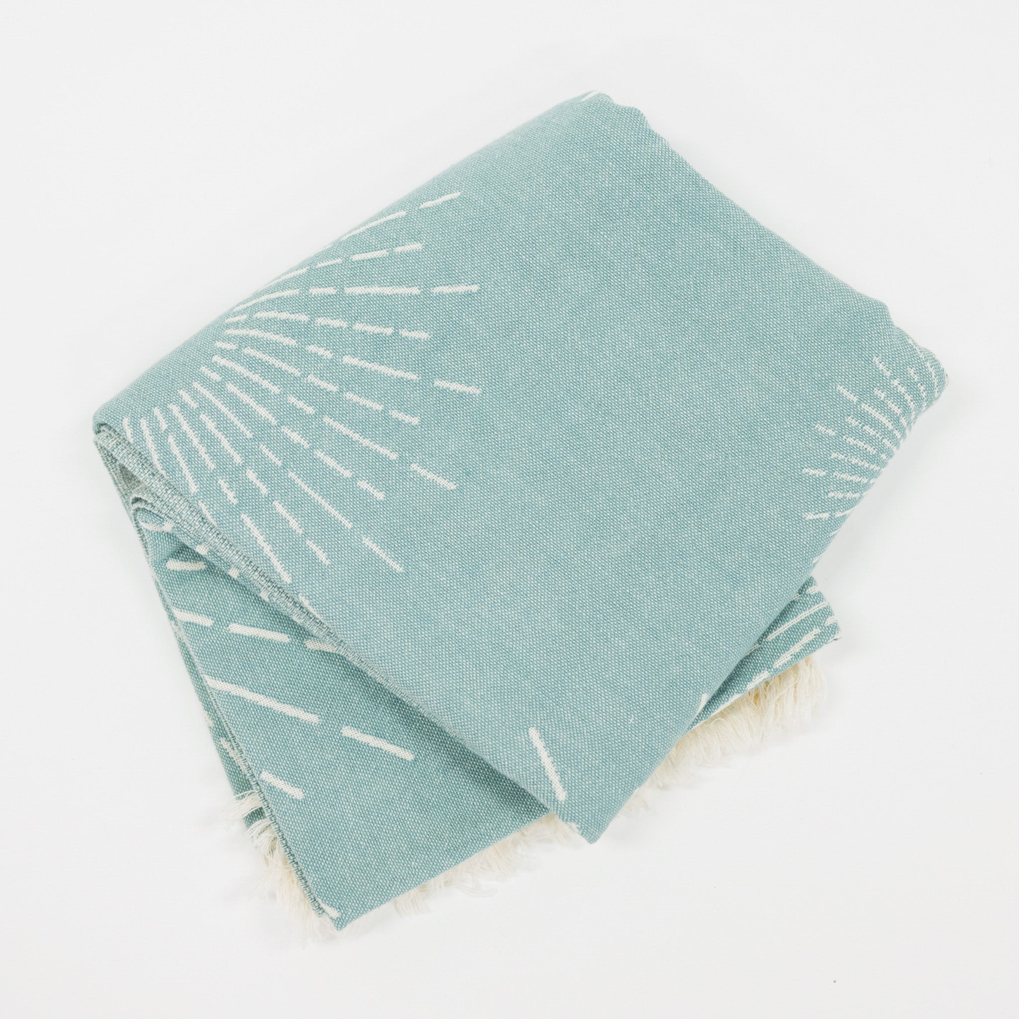 Folded teal beach towel with white abstract patterns on a light gray background