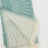 Teal and white patterned beach towel with fringes on a white background