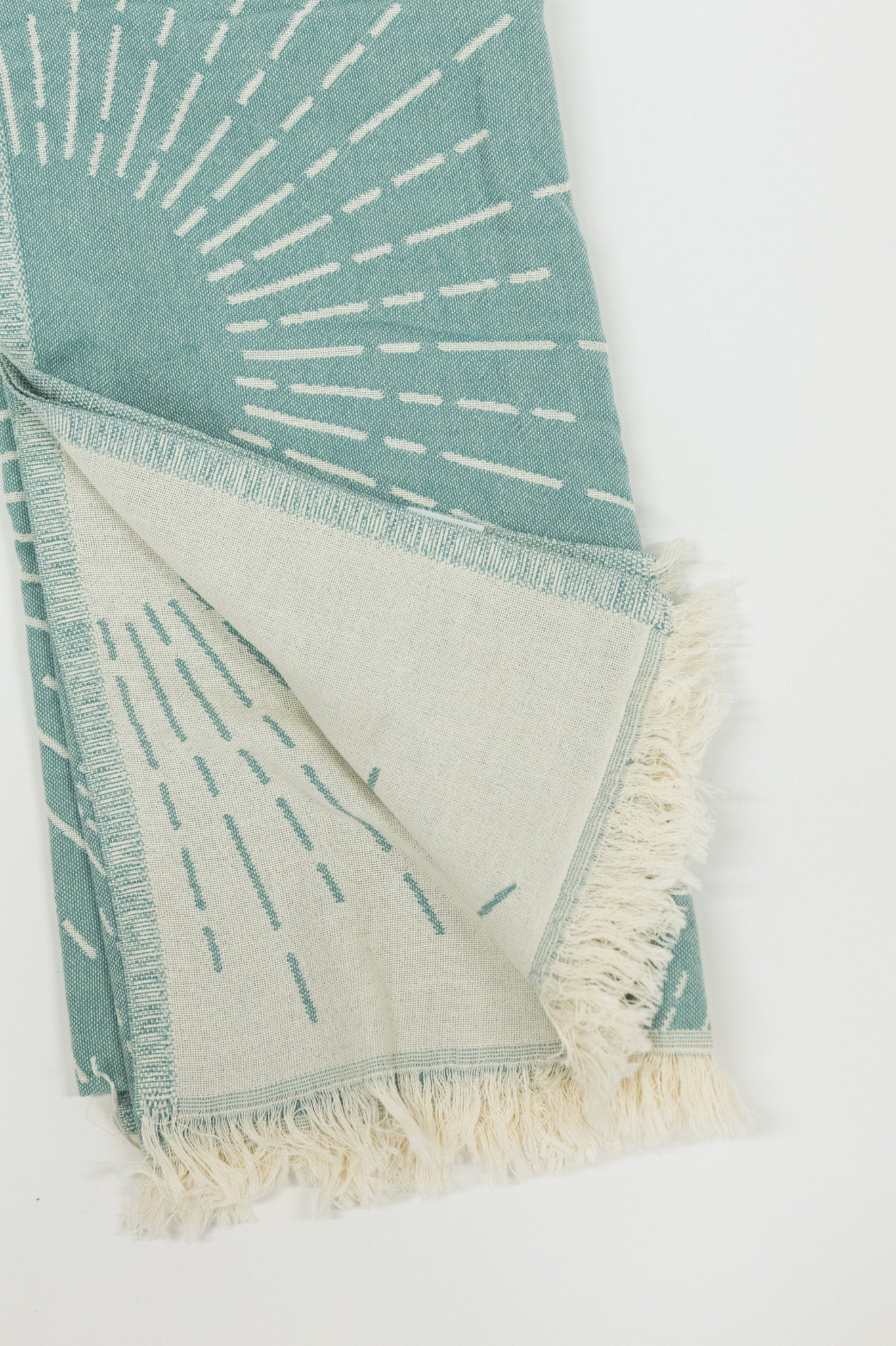 Teal and white patterned beach towel with fringes on a white background