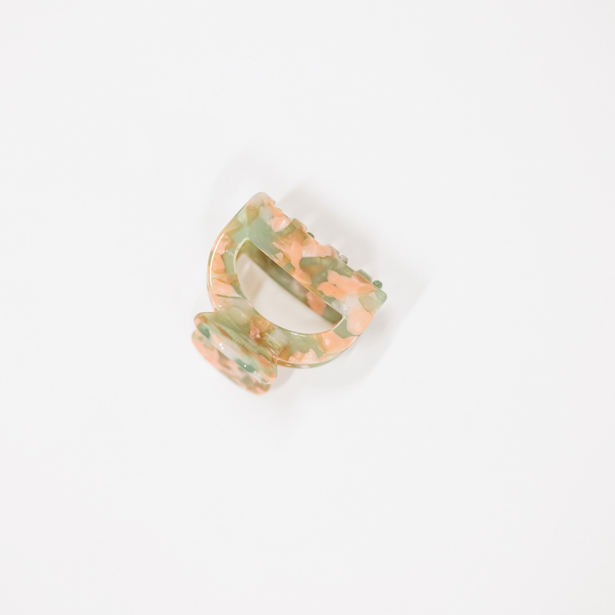 A small tortoiseshell hair claw clip with a marbled pattern of green, peach, and orange, shown on a plain white background.