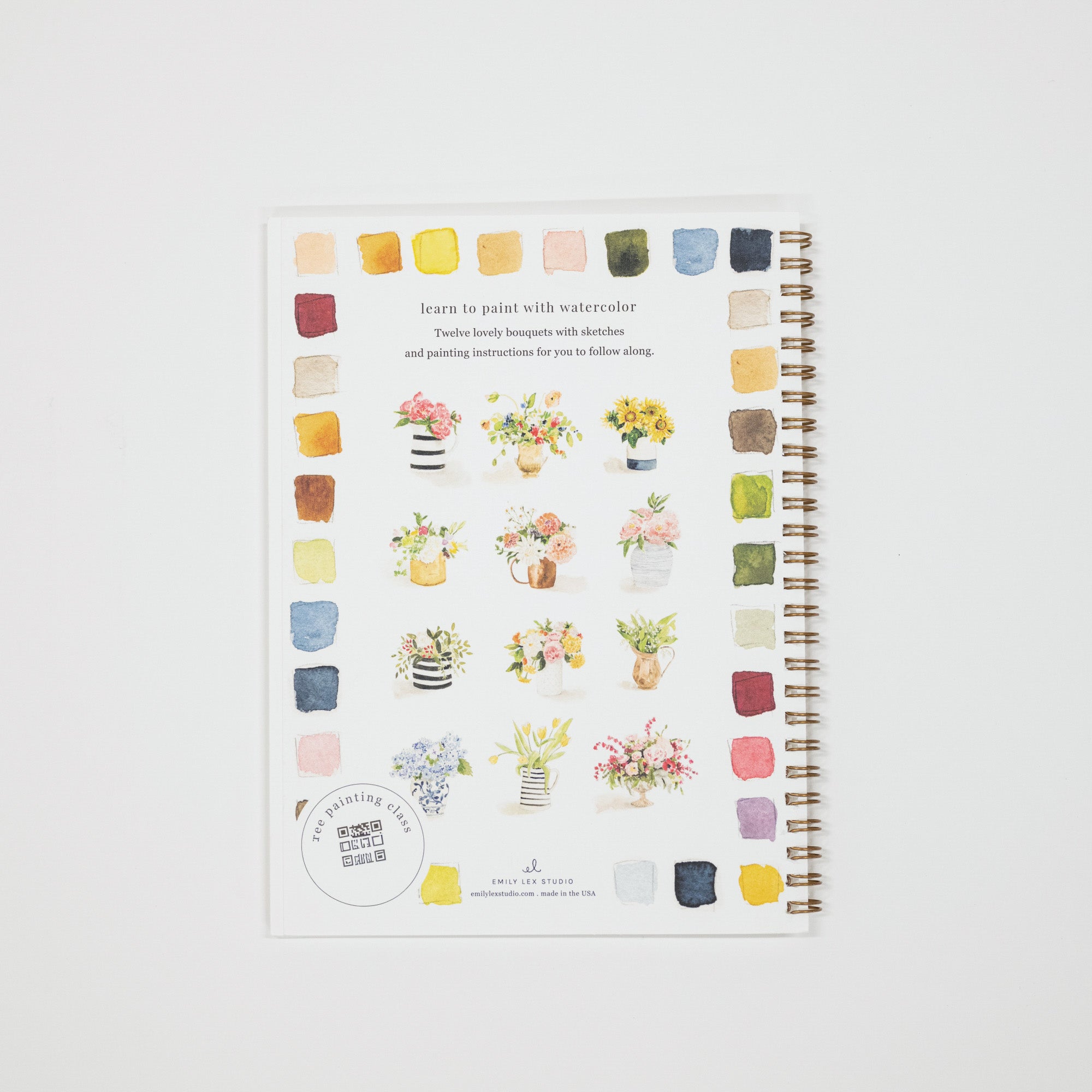 A spiral-bound watercolor painting guide notebook with colorful watercolor swatches and floral illustrations, photographed flat on a light gray background.